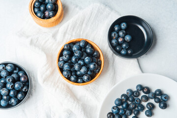 Fresh blueberries in wooden and ceramic bowls on a light surface