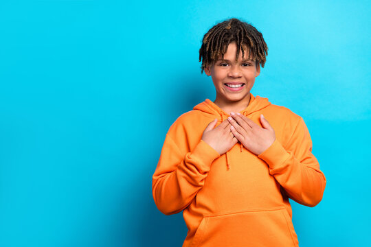 Cheerful schoolboy expressing gratitude in an orange hoodie against a vibrant blue background, displaying joy