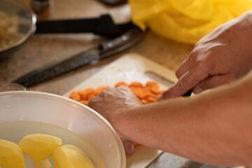 A man prepares vegetables for cooking, peels potatoes and cuts carrots with a knife