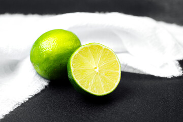 Fresh limes sliced open on a black surface with a white cloth backdrop