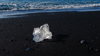 Glittering ice pieces rest on the black volcanic sand at Diamond Beach in Iceland. The stunning...