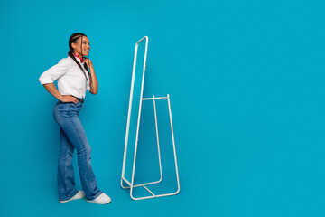 Confident young woman standing near a mirror in casual attire against a blue backdrop, embodying...