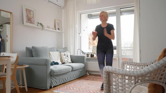Active senior woman doing a low-impact aerobics workout in her living room. This exercise with side steps and arm swings is great for coordination, agility and a safe, joint-friendly cardio.