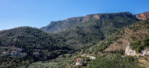 Mountain landscape in Leonidio, Greece. Mount Parnon slopes with olive groves, scattered houses, and cypress trees under blue sky