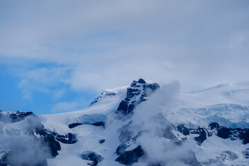 Glacial peaks of Svinafellsjokull Glacier tower above the landscape, partially shrouded in clouds....