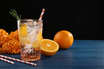 Sparkling water with orange in glass, fresh fruits and straws on blue wooden table, closeup. Space for text