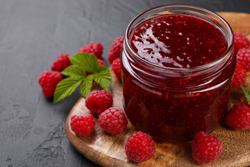 Sweet raspberry jam in glass jar and berries on gray textured table, closeup