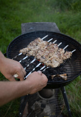 meat on the grill male hands rotate skewers with meat strung on them for even grilling on a...