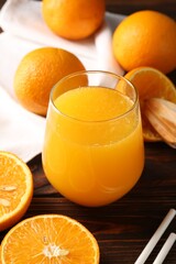 Fresh orange juice in glass, fruits, straws and juicer on wooden table, closeup