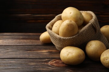 Fresh potatoes in sack on wooden table, closeup. Space for text
