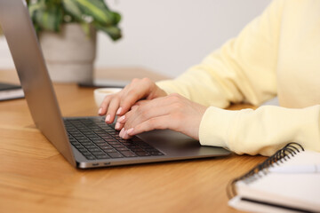 Copywriter using laptop at wooden table indoors, closeup