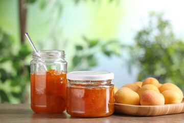 Tasty apricot jam and fresh fruits on wooden table against blurred background, closeup
