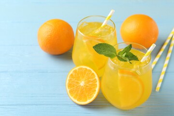 Refreshing soda water with orange slices in glasses, mint, fresh fruits and straws on light blue...