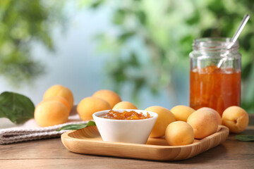 Tasty apricot jam and fresh fruits on wooden table against blurred background, closeup