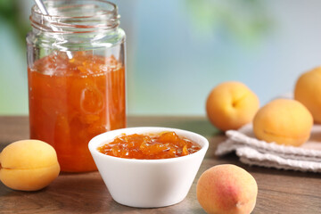Tasty apricot jam and fresh fruits on wooden table against blurred background, closeup