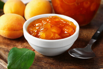 Tasty apricot jam and fresh fruits on wooden table, closeup