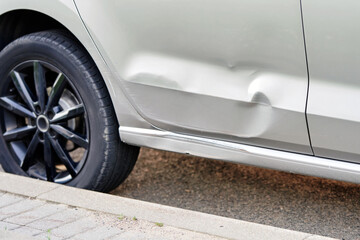 Automobile door panel showing accident damage with dented metal and visible deformation...