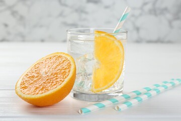 Sparkling water with orange slice in glass and fresh fruit on white wooden table, closeup