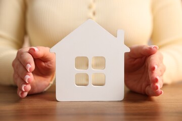 Home security. Woman protecting house figure at wooden table, closeup