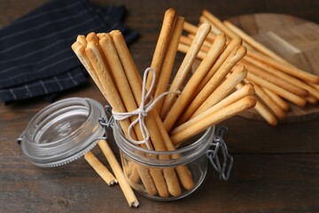 Delicious grissini sticks in open glass jar on wooden table, closeup