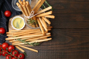 Delicious grissini sticks, fresh tomatoes, rosemary and oil on wooden table, flat lay. Space for text