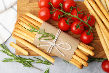 Delicious grissini sticks, rosemary and fresh tomatoes on grey textured table, flat lay