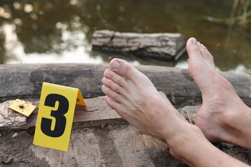 Forensic expertise. Crime scene with dead man's body and marker near lake outdoors, closeup
