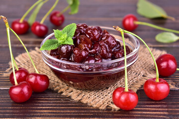 Cherry jam in a glass bowl and fresh cherries on a wooden background. Close-up.

