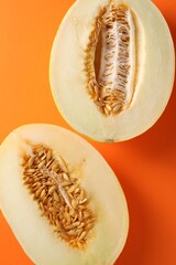Halves of ripe melon on orange background, flat lay