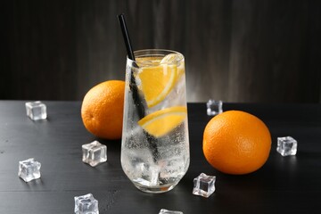 Refreshing soda water with orange slices and ice cubes on black wooden table