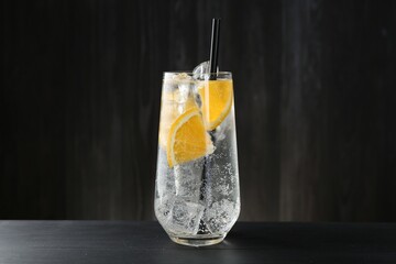 Refreshing soda water with orange slices and ice cubes in glass on black wooden table