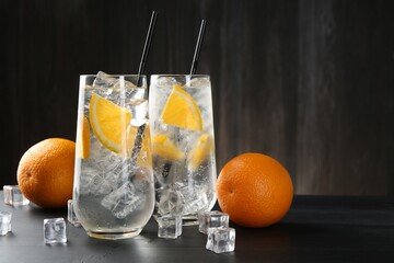 Refreshing soda water with orange slices and ice cubes on black wooden table. Space for text