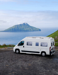 A camper van parked on a scenic overlook in the Faroe Islands, with towering green hills and the...