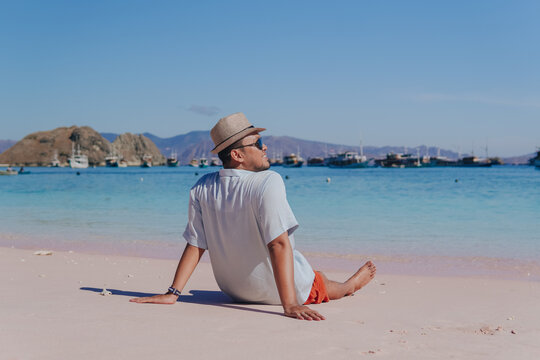 Back view of a young Asian man sitting and enjoying the pink beach scenery in Labuan Bajo.