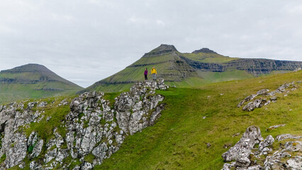 Two hikers stand atop a rocky outcrop on the Gonguturur Hvithamar Trail, surrounded by lush green...