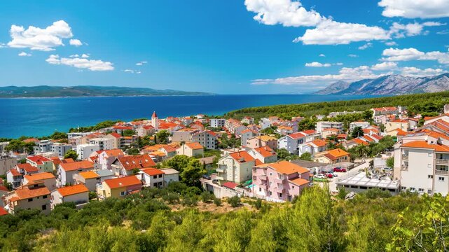 Stunning panoramic timelapse of a coastal town Baska Voda in Croatia, with red-tiled roofs, the blue Adriatic Sea, mountains and clouds ob blue sky