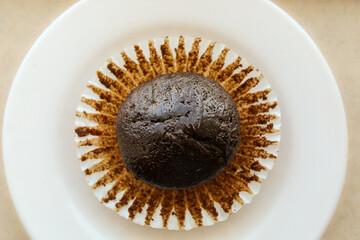 Looking down on a single dark chocolate muffin resting on a white crinkly paper liner. Abstract...