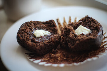 A moist chocolate muffin or cupcake, cut in half and placed on a white plate with a paper liner....