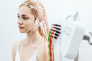Young woman with blonde hair wearing a medical headset is undergoing a brainwave analysis procedure...