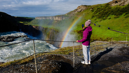 A traveler captures the majestic Gullfoss waterfall in Iceland, with a vibrant rainbow forming in...