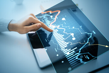 Business hand analyzing digital financial chart with currency and stock market data on a futuristic holographic display interface on tablet screen.