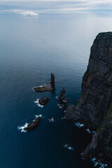 Majestic cliffs rise dramatically from the tranquil Atlantic waters of the Faroe Islands, adorned...