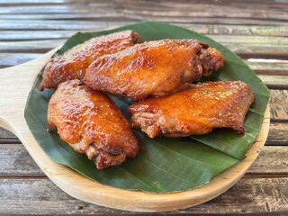 Close-up of grilled chicken wings served on a banana leaf, traditional Thai street food with golden crispy skin and smoky