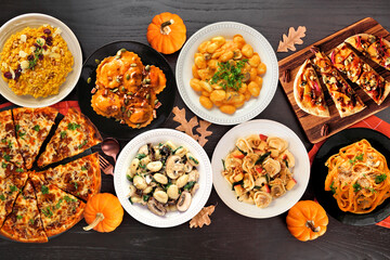 Delicious autumn meal table scene. Top view on a black wood background. Pumpkin and apple theme risotto, pasta, gnocchi, flat bread and pizza.