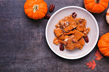 Autumn pumpkin spice pecan brittle candy. Above view on a plate against a dark stone background....