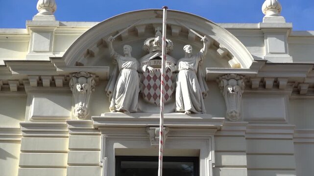 Close up of the Principality's coat of arms with two monks and the motto carved on the facade of the Palace of Justice. Translation: "God willing", Monaco