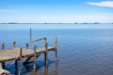 Wooden pier extending over calm lake water under clear blue sky.