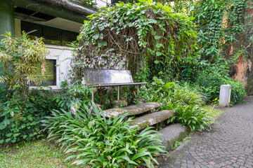 A quiet, empty bench sits amidst lush, vibrant tropical foliage and dense greenery, offering a...