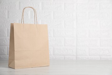 Kraft paper bag on grey wooden table near white brick wall. Space for text