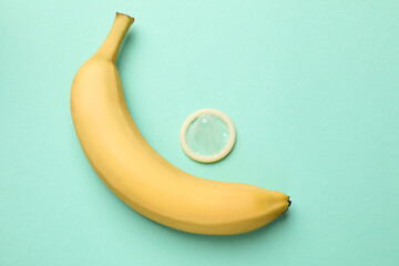 Sex education. Banana and condom on turquoise background, flat lay